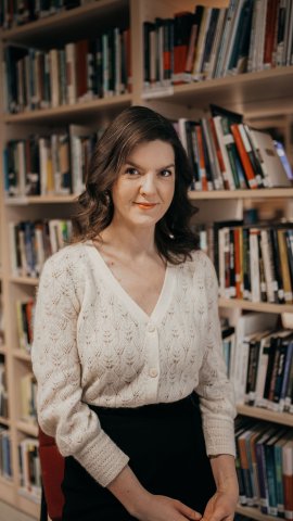 Pildil on naine istumas raamaturiiuli taustal